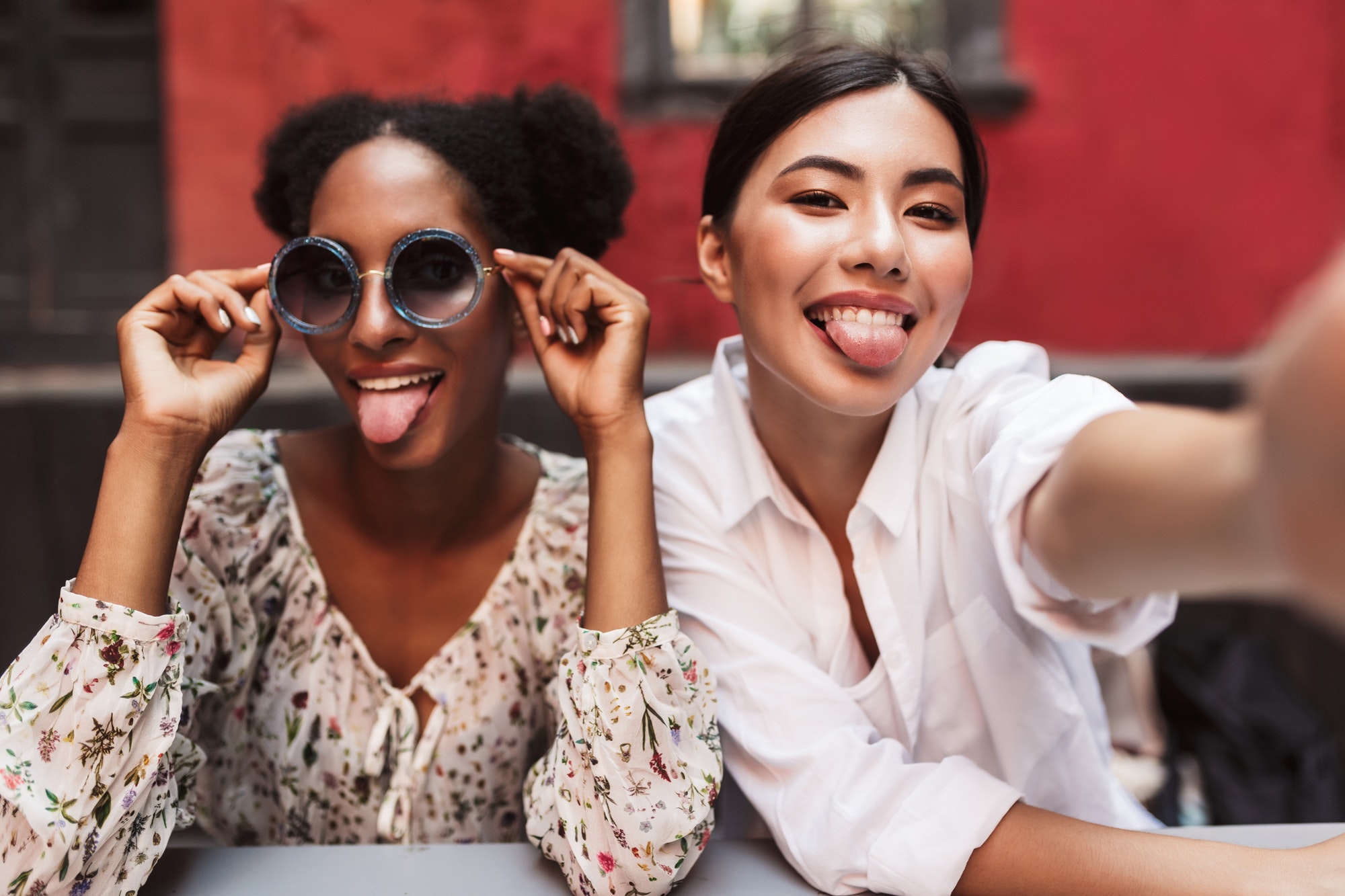 Two pretty girls happily showing tongues while taking photos tog