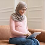 Side View Of Pregnant Muslim Female Using Tablet At Home